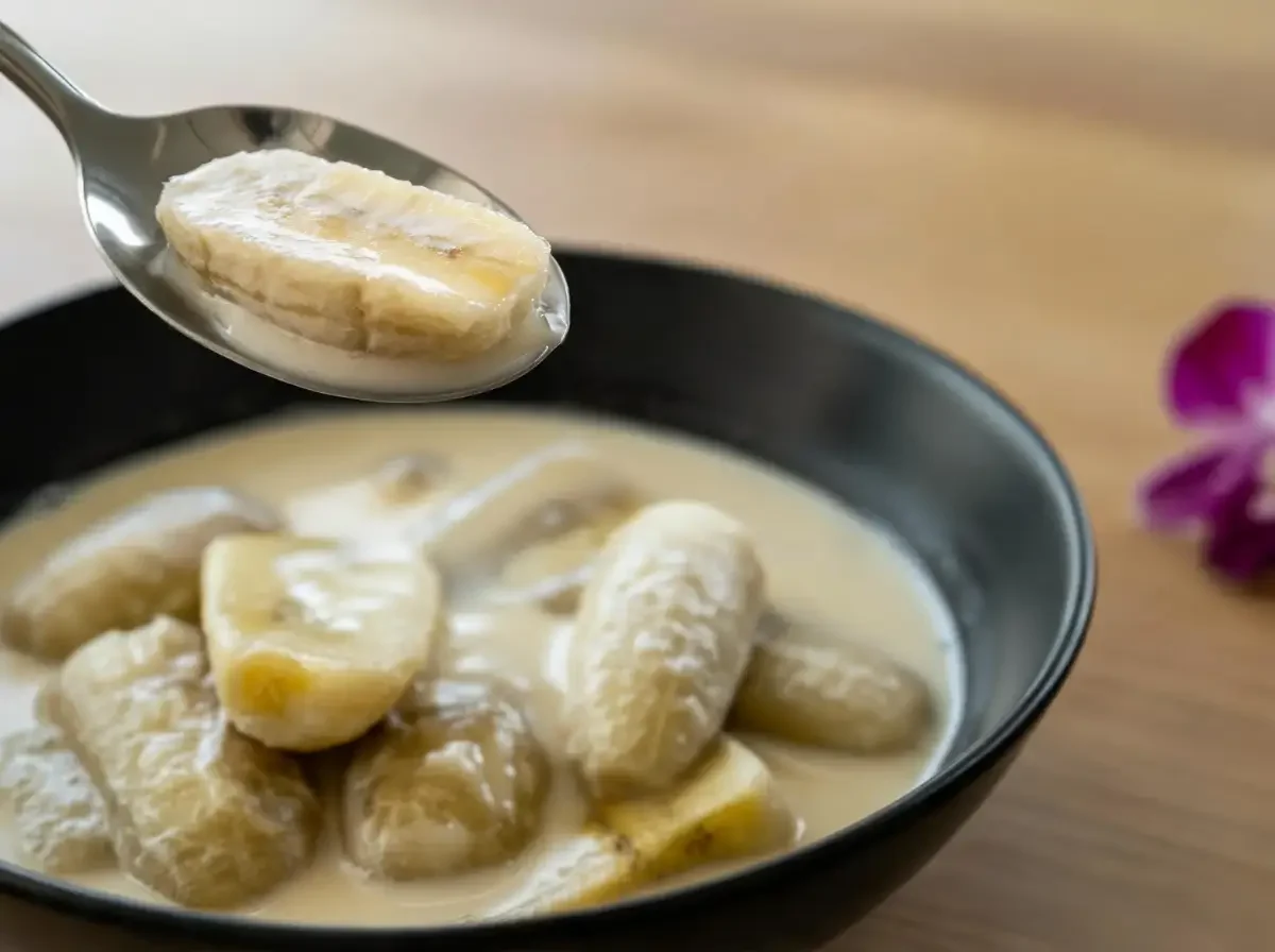 Ein Löffel präsentiert ein Stück des traditionellen thailändischen Desserts Bananen in Kokosmilch.