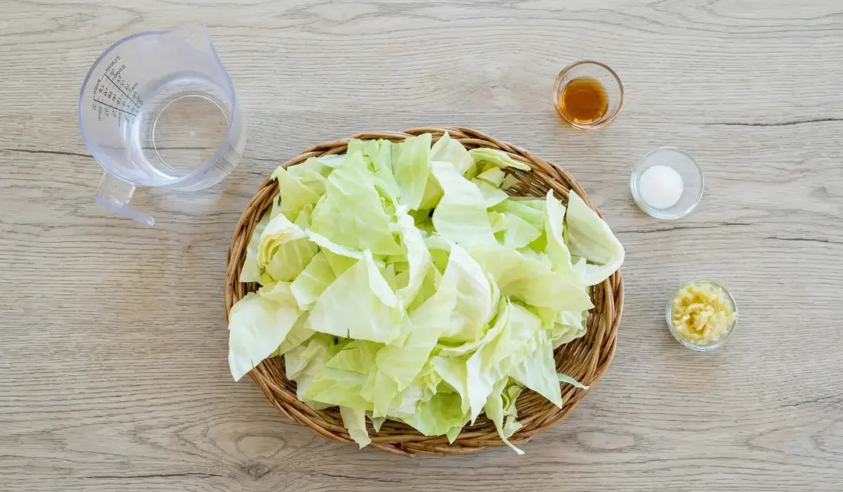 Vorbereitete Zutaten für das Gericht Gebratener Spitzkohl mit Fischsauce: Roher Kohl, Wasser, Fischsauce, Zucker und Knoblauch auf einem Holztisch.