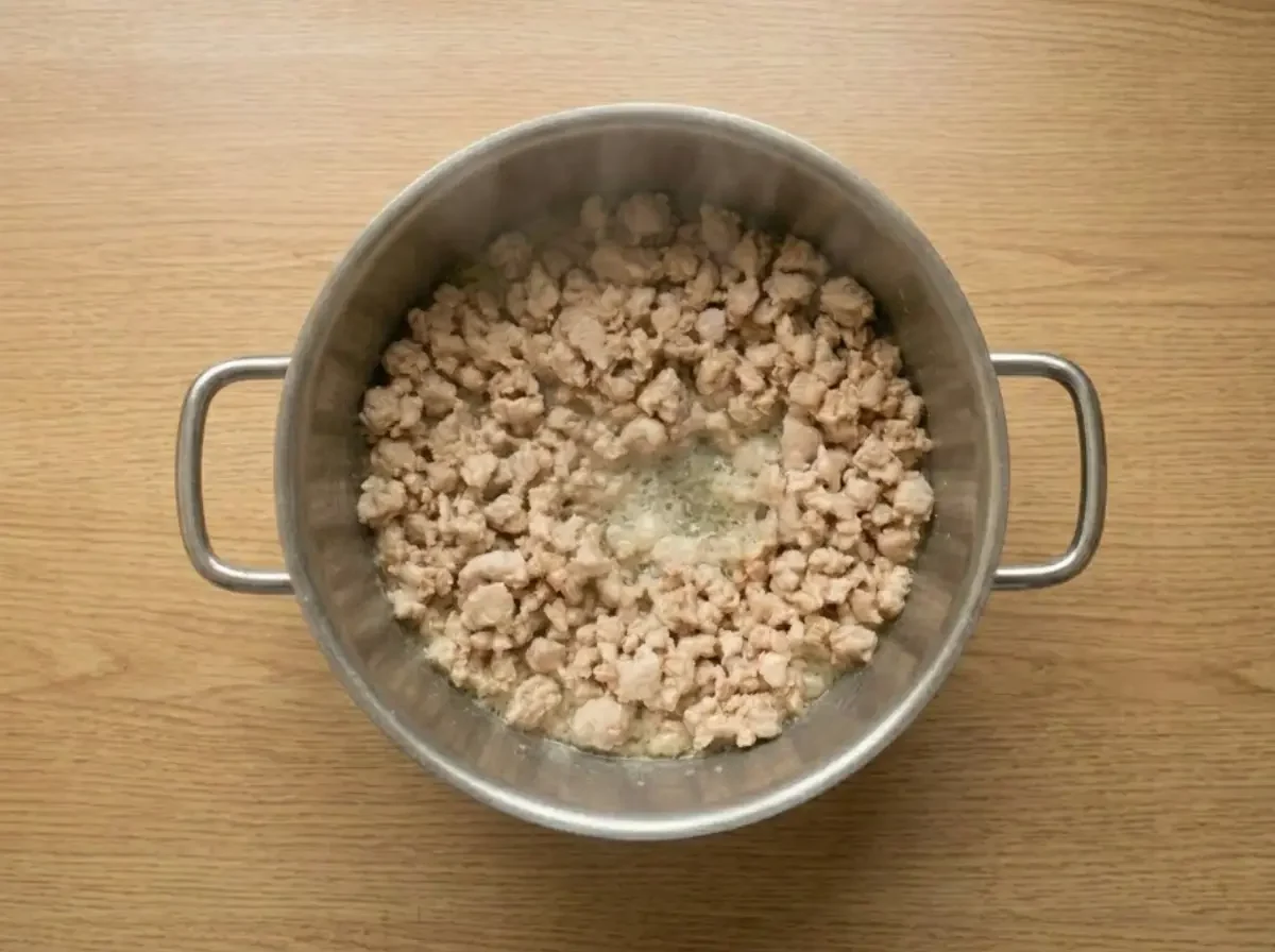 Ein Edelstahltopf von oben betrachtet, in dem gerade das Schweinehackfleisch für den Nam Sod gart. Das Fleisch köchelt im eigenen Saft und leichter Dampf steigt auf.