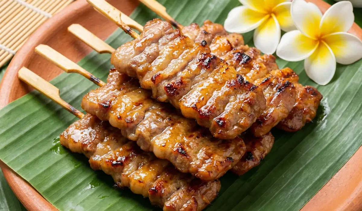 Moo Ping Spieße mit glänzender Marinade auf Bananenblatt serviert, dekoriert mit weißen tropischen Blüten