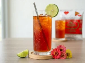 Ein Glas fertiger Cha Manao, garniert mit einer frischen Limettenscheibe. Im Hintergrund ist die originale Cha Tra Mue Teemischung zu sehen.