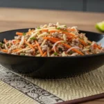 Ein schwarzer Teller mit Nam Sod, Thai Salat mit Schweinefleisch und Ingwer.