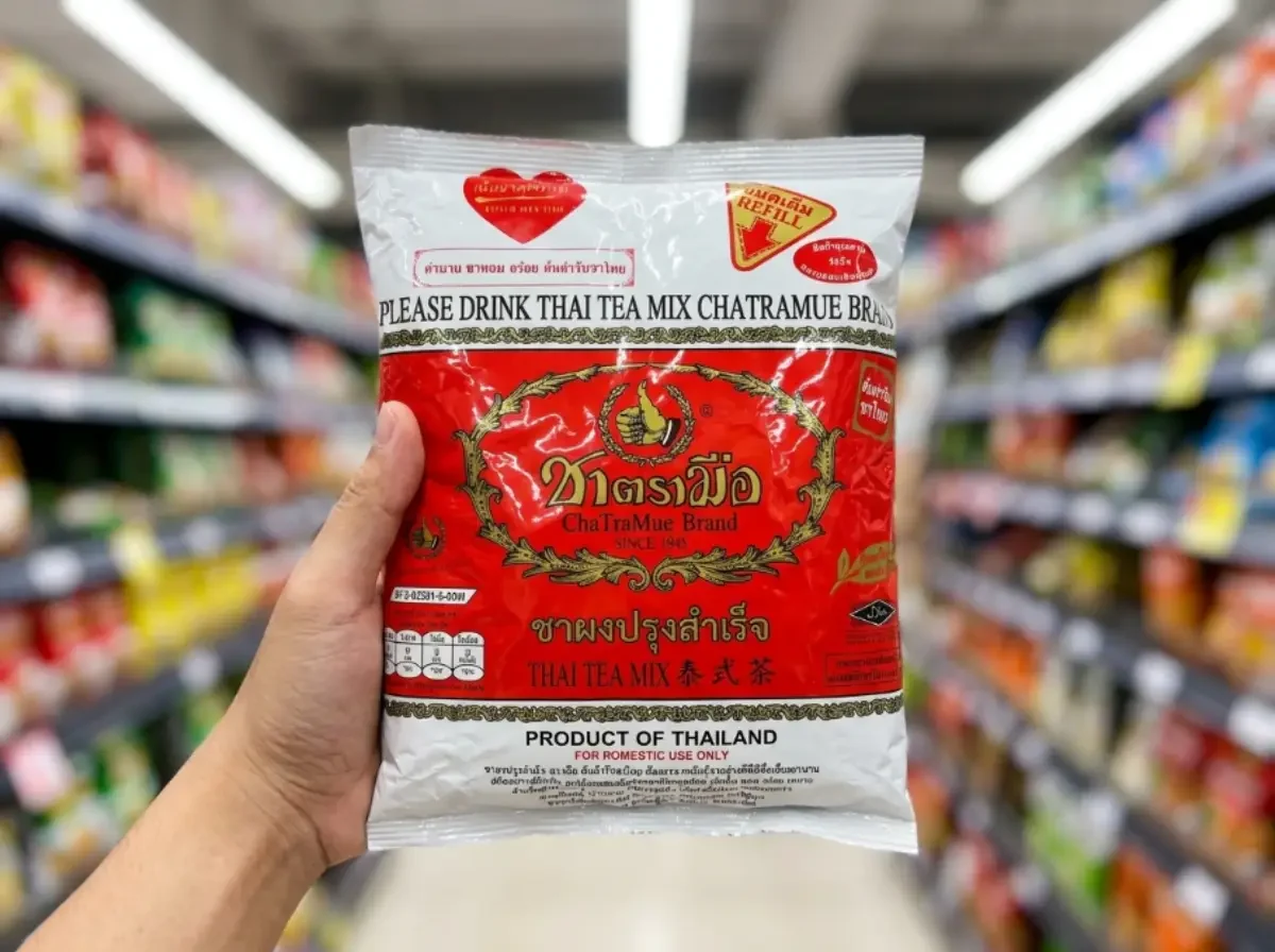 Eine Hand hält die rote Packung der originalen Cha Tra Mue Teemischung, die man für authentischen Cha Manao benötigt, in einem Asiamarkt.
